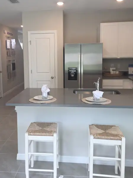 A sleek kitchen with a gray countertop island, stainless steel fridge, and elegant seating for two. A sleek kitchen with a gray countertop island, stainless steel fridge, and elegant seating for two.
