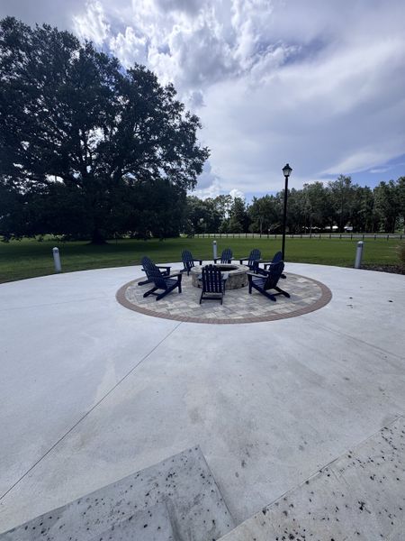 A serene outdoor firepit area with Adirondack chairs surrounded by lush greenery in Granary Park by Lennar (Green Cove Springs, FL).