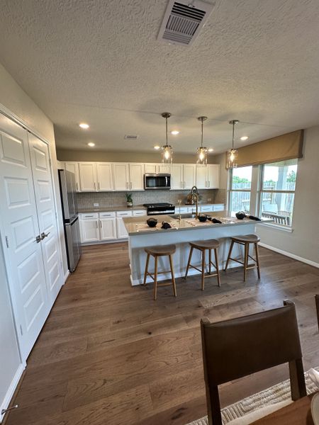 A modern kitchen with white cabinets, an island with stools, and warm wood flooring.