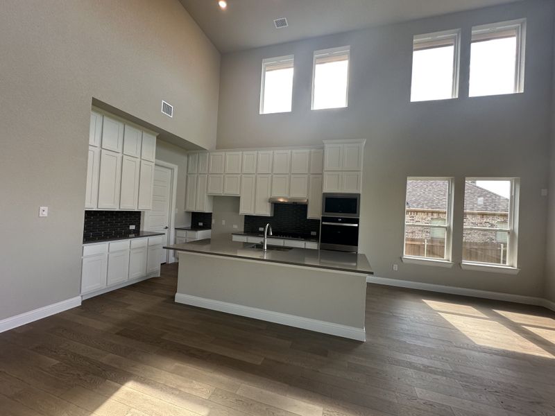 An airy kitchen with high ceilings, large windows, white cabinetry, and a center island, featuring sleek hardwood flooring. An airy kitchen with high ceilings, large windows, white cabinetry, and a center island, featuring sleek hardwood flooring.