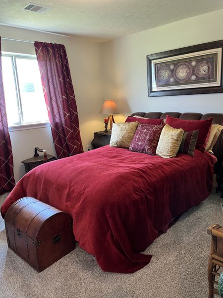 A cozy bedroom featuring a rich red bed set, elegant decor, and soft carpeting for a warm ambiance.