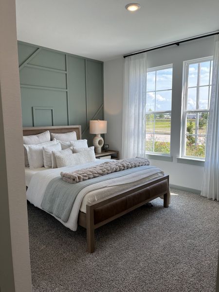 A serene bedroom with a paneled accent wall, plush bedding, and large windows for ample natural light.