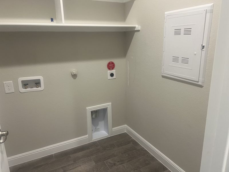 A laundry area with hookups, gray walls, built-in shelving, and wood-look flooring. A laundry area with hookups, gray walls, built-in shelving, and wood-look flooring.