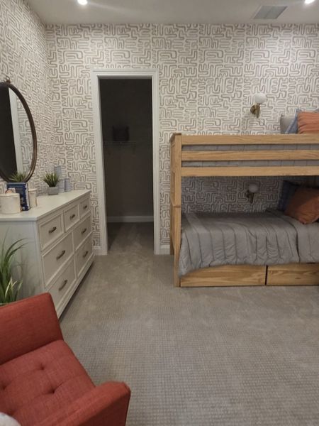 A cozy bedroom with patterned wallpaper, a wooden bunk bed, red armchair, and sleek dresser.