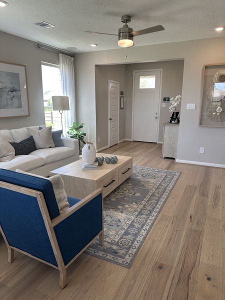 A cozy living area with light wood flooring, elegant decor, and a modern ceiling fan, creating a welcoming atmosphere.