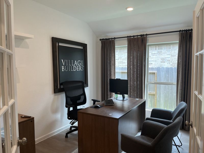 A cozy home office featuring a sleek desk, plush seating, and a statement wall art piece labeled "Village Builders."