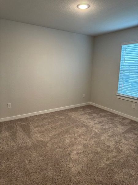 An empty room with neutral carpet, soft beige walls, a recessed light, and a window with blinds. An empty room with neutral carpet, soft beige walls, a recessed light, and a window with blinds.
