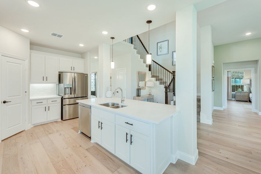 Kitchen with white cabinets, center island with sink, stainless steel appliances, and light hardwood floors open to staircase Kitchen with white cabinets, center island with sink, stainless steel appliances, and light hardwood floors open to staircase