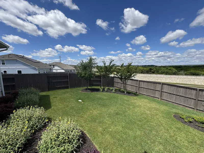 A lush backyard with manicured lawn and wooden fencing in Cloverleaf by Brohn Homes (Austin, TX).