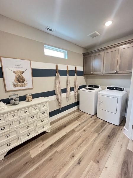 A charming laundry room with wooden floors, striped accent wall, and cozy decor featuring a modern washer and dryer. A charming laundry room with wooden floors, striped accent wall, and cozy decor featuring a modern washer and dryer.