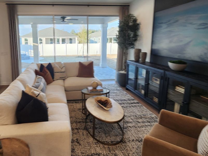 A cozy living room with a cream sectional, modern decor, and large sliding glass doors opening to a bright backyard view.