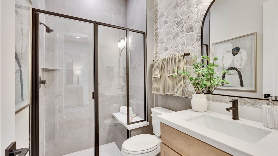 Experience elegance with a glass shower, stone accent wall, and arched mirror in Lakeside Meadows. Experience elegance with a glass shower, stone accent wall, and arched mirror in Lakeside Meadows.