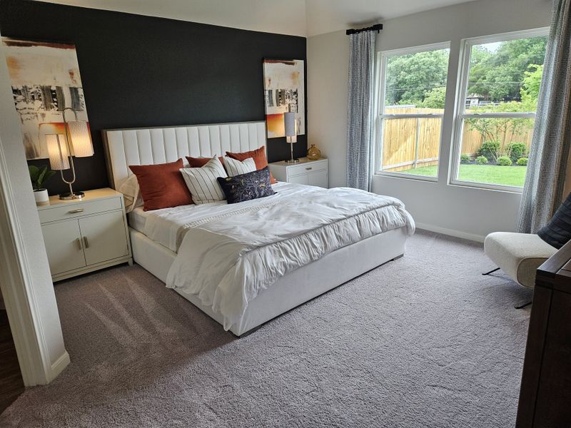 Elegant bedroom featuring a dark accent wall, plush white bedding, and large windows overlooking a serene backyard garden.
