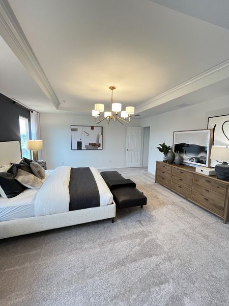 A spacious bedroom with a cozy bed, elegant chandelier, and modern art. A wooden dresser adds warmth to the neutral decor. A spacious bedroom with a cozy bed, elegant chandelier, and modern art. A wooden dresser adds warmth to the neutral decor.