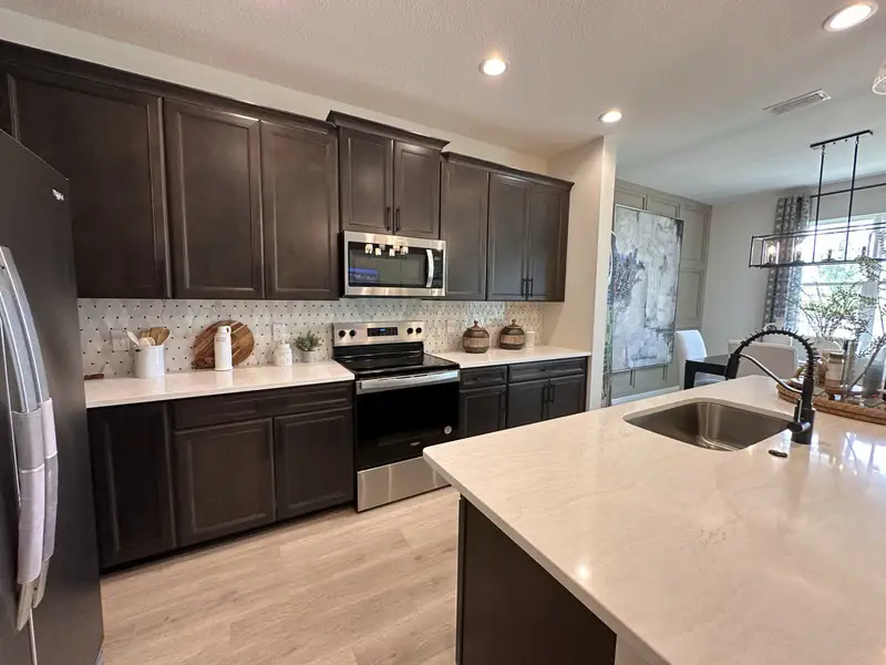 A modern kitchen featuring dark cabinets, a patterned backsplash, and sleek countertops with stainless steel appliances.