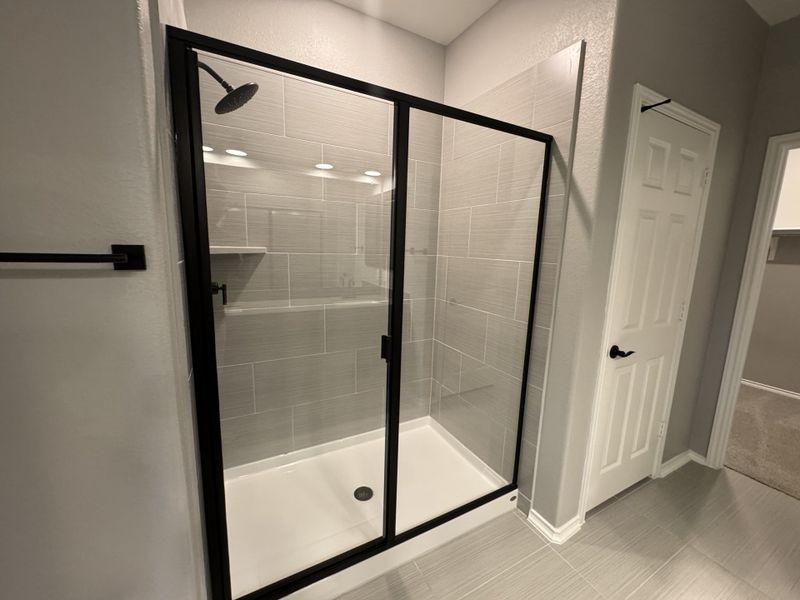 A sleek bathroom features a modern glass shower with dark framing, gray tile, and elegant lighting.