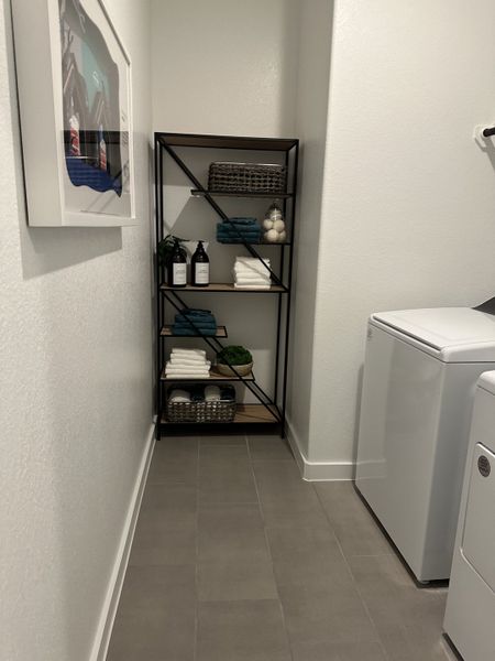 A modern laundry room featuring sleek shelving with towels, decor, and essentials, paired with a washing machine and dryer. A modern laundry room featuring sleek shelving with towels, decor, and essentials, paired with a washing machine and dryer.
