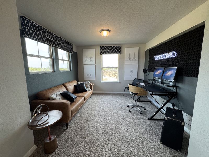 A cozy recording studio with a leather sofa, accented walls, dual monitors, and unique art pieces creating a stylish workspace.