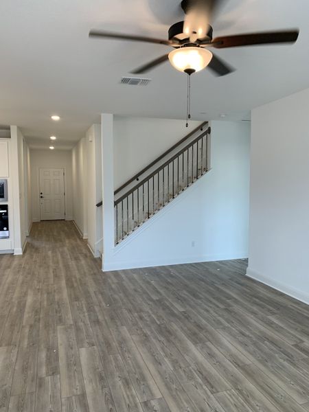 An open living space with wood floors, a ceiling fan, and a sleek staircase creates a modern and inviting atmosphere.
