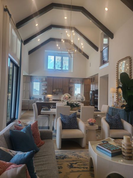 A spacious living area with vaulted ceilings, elegant chandelier, cozy seating, and a chic kitchen.