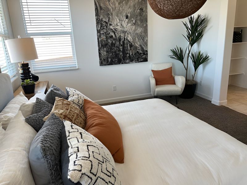 A cozy bedroom with a plush bed, decorative pillows, and modern art, complemented by a comfy chair and potted plant. A cozy bedroom with a plush bed, decorative pillows, and modern art, complemented by a comfy chair and potted plant.