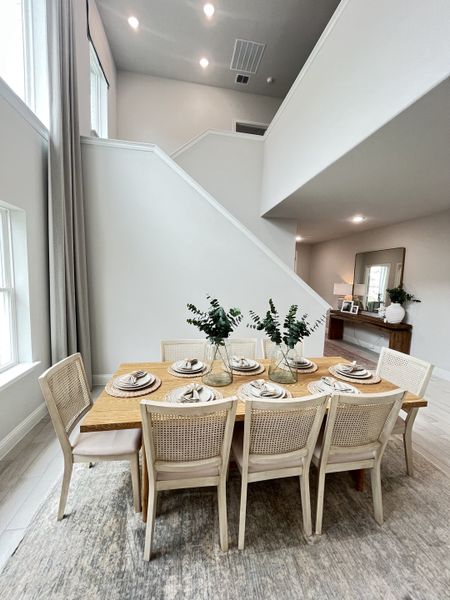 A spacious dining area with a wooden table, elegant chairs, and high ceilings, exuding modern simplicity and warmth.