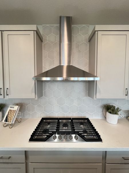 A modern kitchen with hexagonal tile backsplash, sleek stainless-steel range hood, and chic cabinetry.