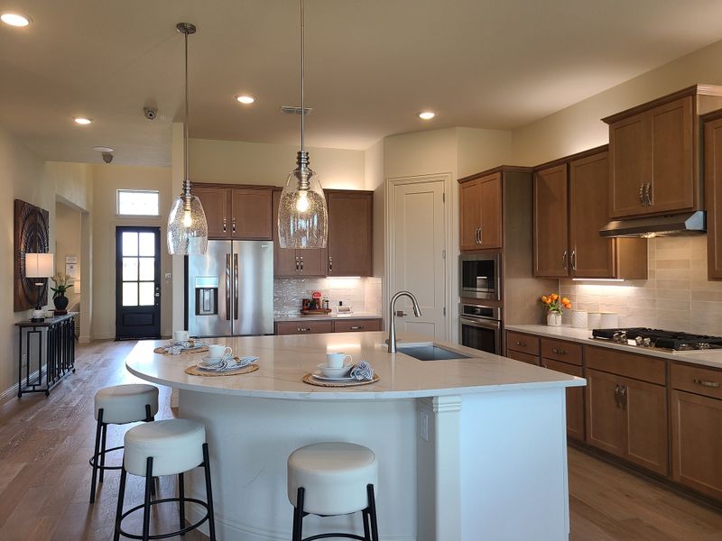 A modern kitchen with warm wood cabinets, a sleek island, pendant lighting, and stainless steel appliances.