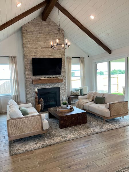 A cozy living room with a stone fireplace, vaulted ceiling, modern chandelier, and elegant sofas on a patterned rug.