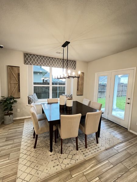 A bright dining room with a dark wood table, beige chairs, and modern chandelier, featuring wood floors and natural light.