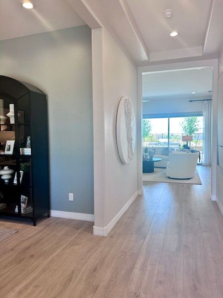 A bright hallway with light wood flooring, leading to a cozy living room with large windows and modern decor.