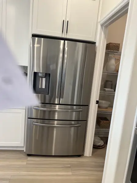 A modern kitchen showcasing a sleek stainless-steel fridge, white cabinetry, and a neatly organized pantry.