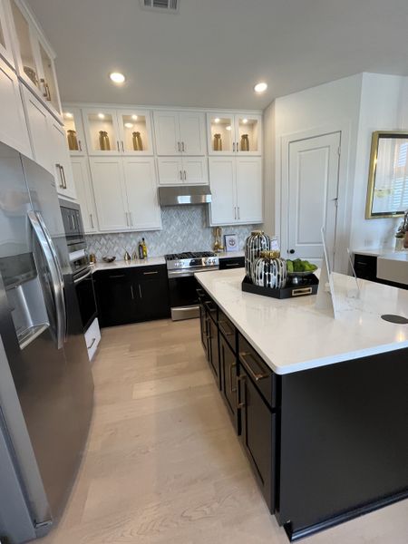 A modern kitchen featuring white cabinets, a sleek island, and stainless steel appliances, accented by elegant lighting.