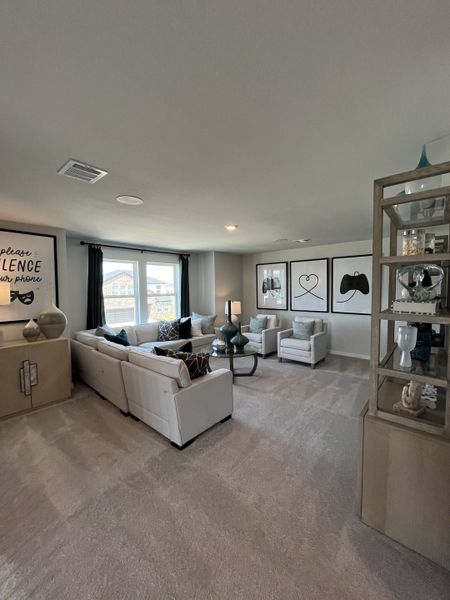 A cozy living room with plush beige carpet, a sectional sofa, modern art, and ample natural light.