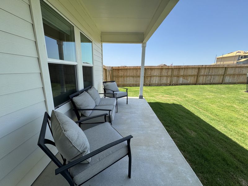 A cozy patio with cushioned seating, overlooking a fenced yard and vibrant lawn.