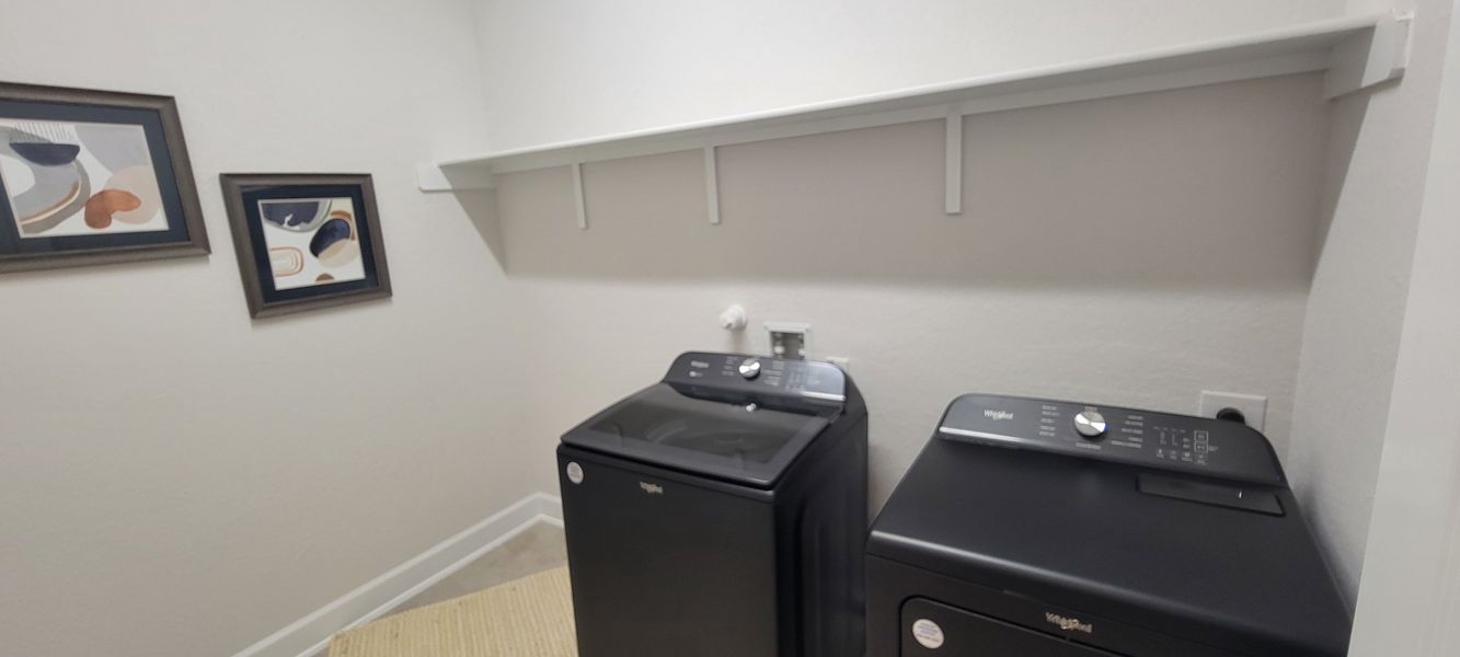 A modern laundry room featuring sleek black appliances, abstract wall art, and a convenient shelf.