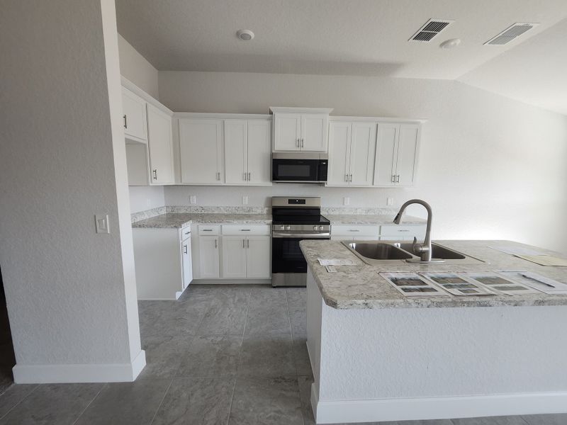 A modern kitchen with granite countertops, white cabinetry, stainless steel appliances, and tile flooring.