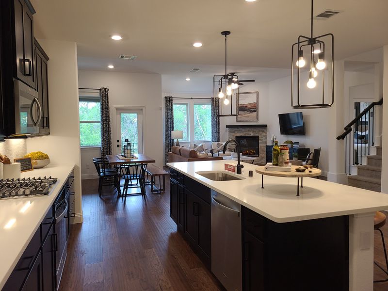 A modern kitchen and living area with dark cabinets, sleek countertops, and elegant lighting, leading to a cozy seating space. A modern kitchen and living area with dark cabinets, sleek countertops, and elegant lighting, leading to a cozy seating space.