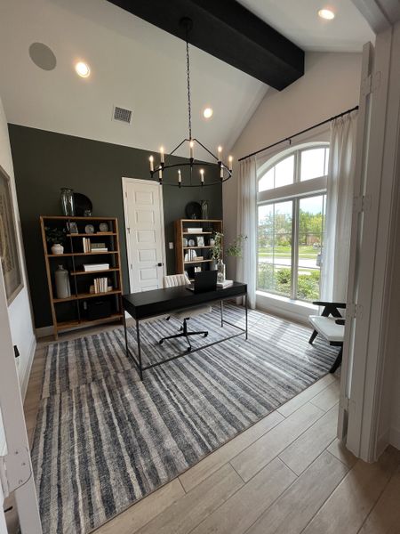 A sophisticated home office with vaulted ceiling, black chandelier, and large window for natural light.