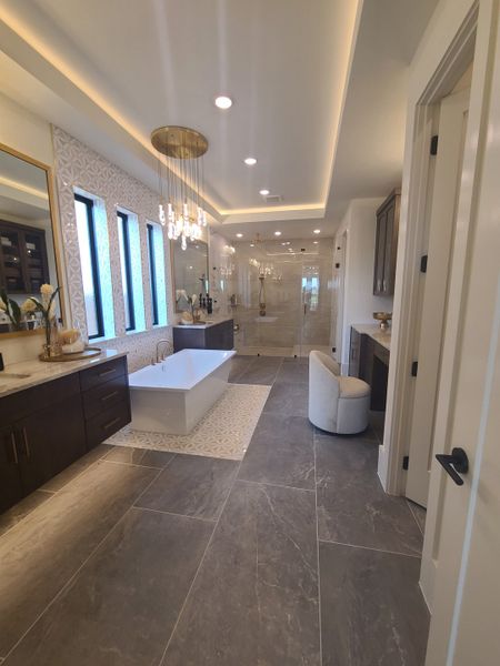 A luxurious bathroom featuring a freestanding tub, elegant chandelier, and spacious shower with modern finishes.