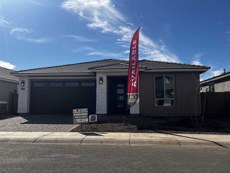 A stylish house with a light garage, stone accents, and and a paved driveway, set in a sunny neighborhood.