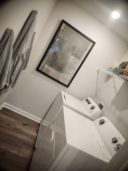 A modern laundry room featuring sleek appliances, neutral walls, framed art, and soft lighting for a clean, functional space.