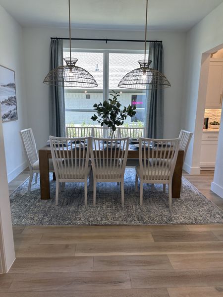 A charming dining room with a wooden table, white chairs, woven pendant lights, and floor-to-ceiling window curtains. A charming dining room with a wooden table, white chairs, woven pendant lights, and floor-to-ceiling window curtains.