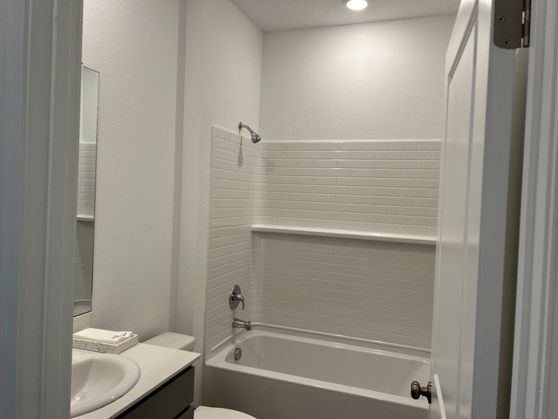 A modern bathroom with a sleek tub-shower combo, white tiled walls, and a compact vanity.