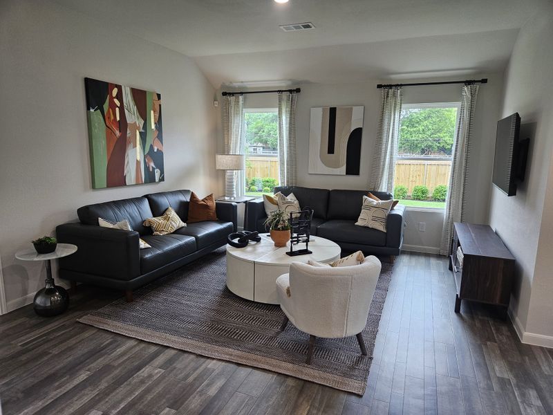 A cozy living room with dark leather sofas, abstract art, and a circular coffee table on a textured rug.