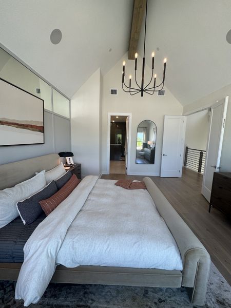 A modern bedroom with vaulted ceilings, elegant chandelier, cozy bedding, and a minimalist design.