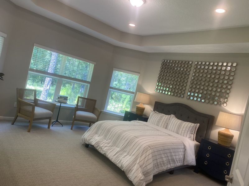 A serene bedroom with a plush bed, cozy seating area, and soft natural light streaming through large windows. A serene bedroom with a plush bed, cozy seating area, and soft natural light streaming through large windows.
