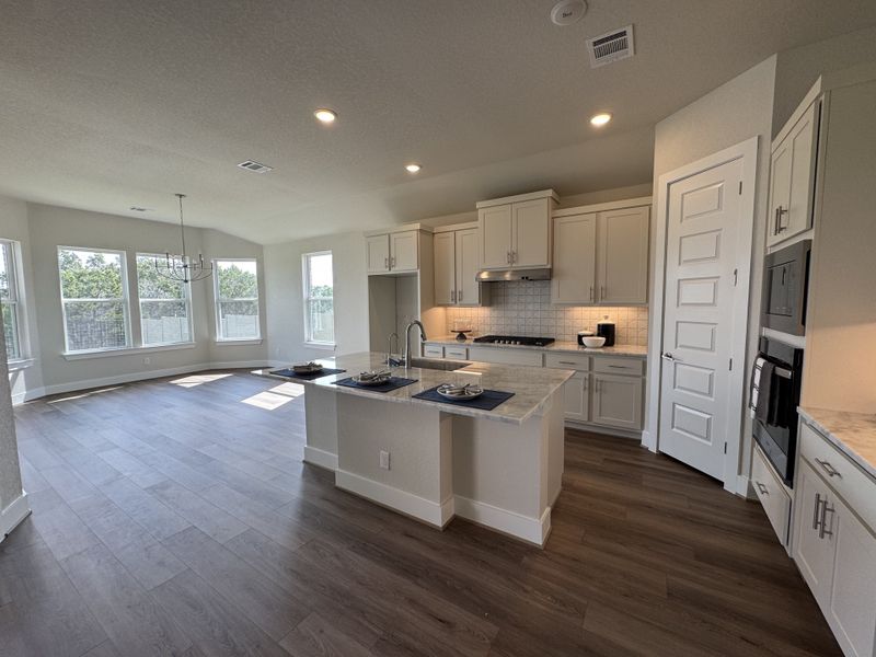 A spacious kitchen with white cabinetry, island seating, and bright windows, opening to a dining area with modern lighting.