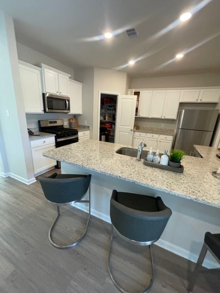 A modern kitchen featuring granite countertops, sleek bar stools, white cabinetry, and stainless steel appliances.