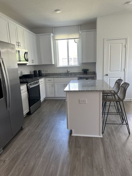 A modern kitchen featuring sleek appliances, white cabinetry, granite countertops, and stylish bar stools.